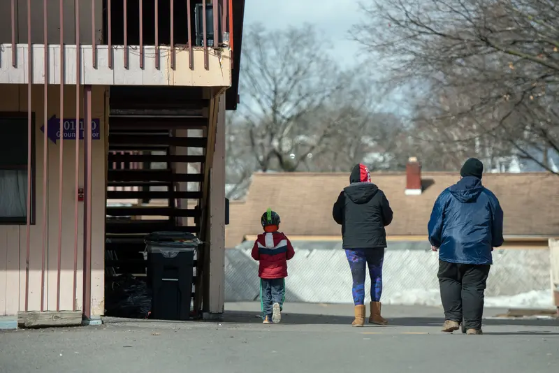 A child and two adults wearing winter coats walk away from the camera near the Knights Inn in Endwell, New York.