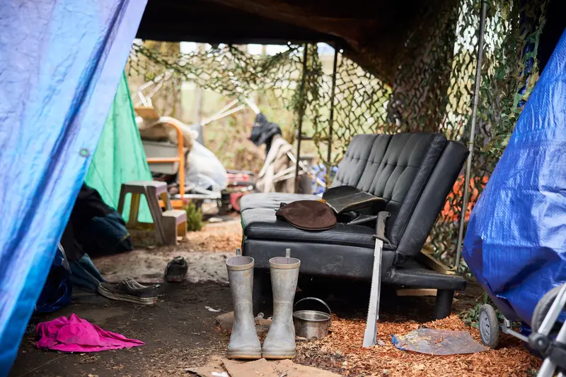 A couch, clothes, rain boots, shelves and kitchen supplies sit underneath tarps and fencing.