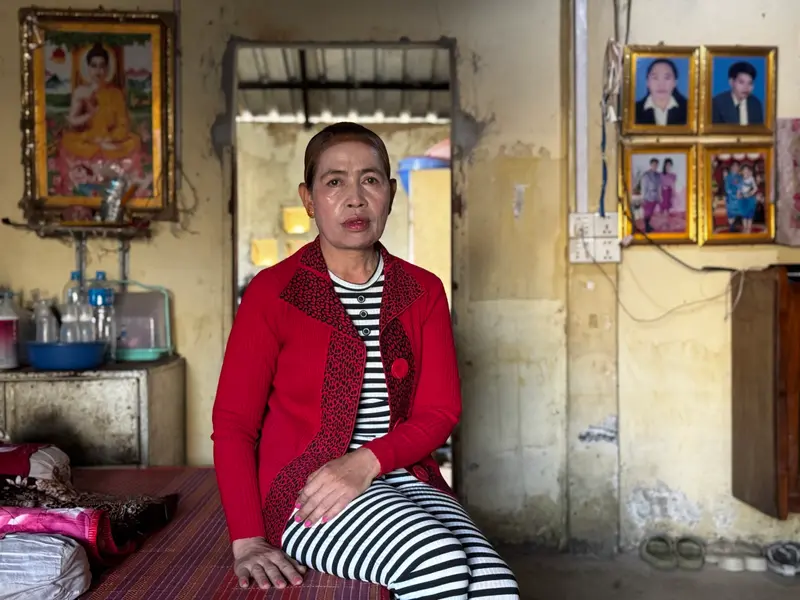 Une femme qui porte une veste rouge sur une chemise et un pantalon noir et blanc se trouve dans une pièce avec des murs jaunes et des portraits encadrés.