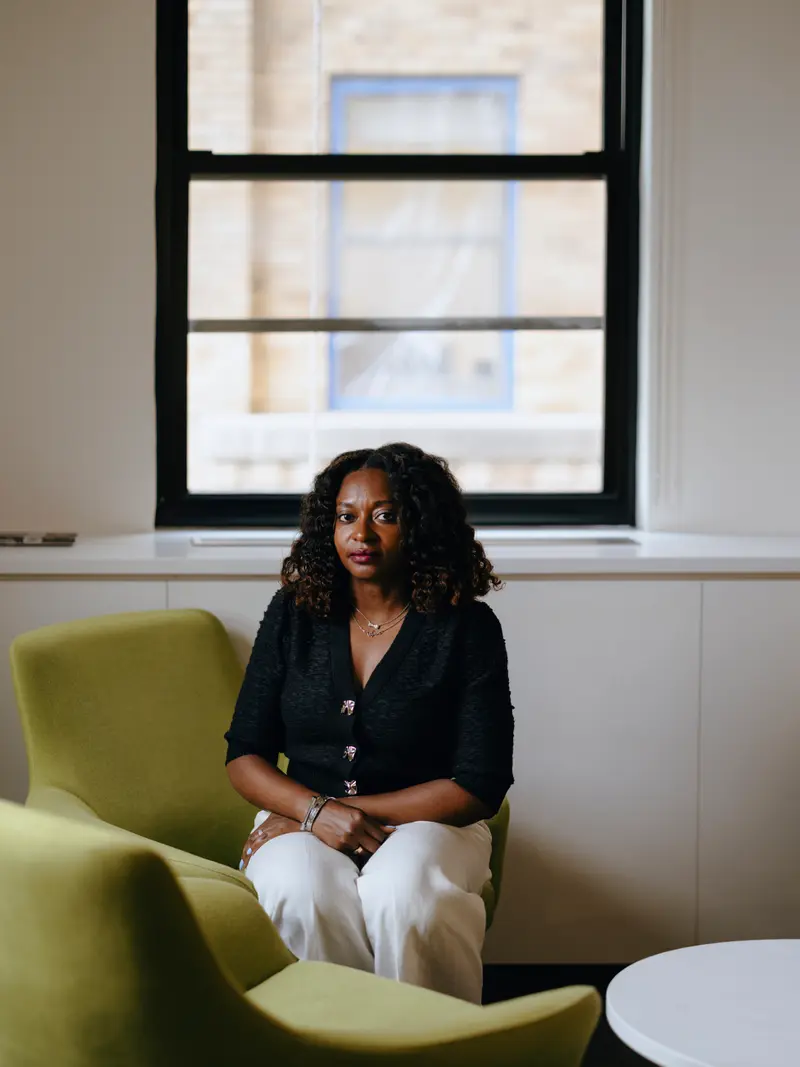 A woman sitting in a green plush arm chair with her hands folded on her lap.