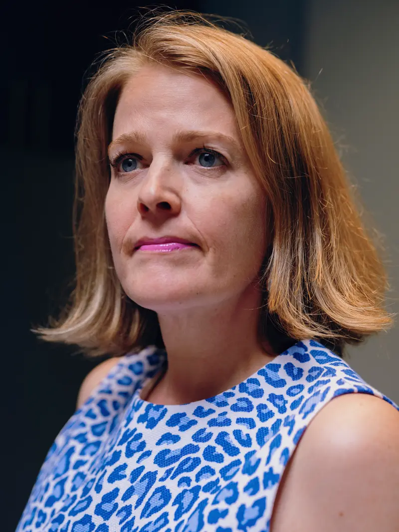 A closeup of a woman with red hair and blue eyes looking up, wearing a blue animal-print shirt.
