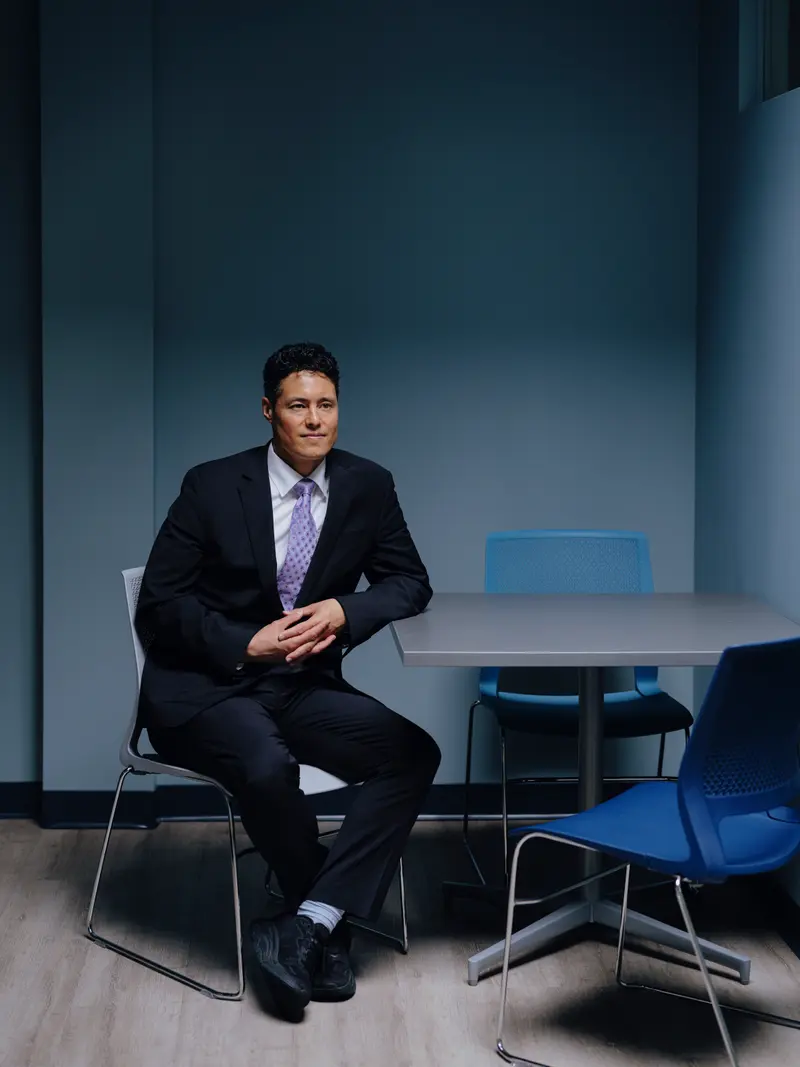A man with short curly hair wearing a black suit and purple tie.