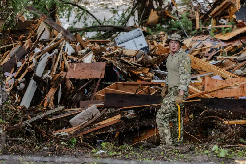 Première photo: Deux hommes en débardeur, shorts et tongs sont mis à l'ombre par un réservoir de carburant qui est tombé de l'autre côté de la rue et a enlevé des lignes électriques. Deuxième image: Un homme en uniforme camouflage fait un tas massif de résidus de bois, de métal et de plastique.