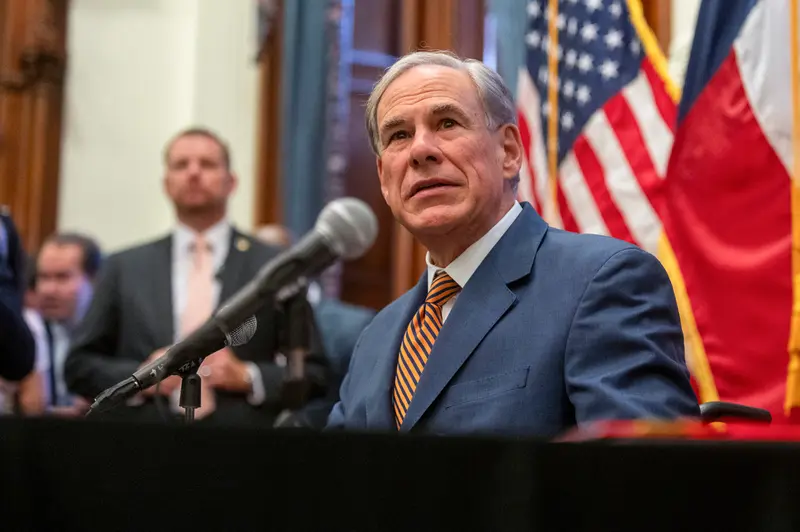Gov. Greg Abbott speaks into a microphone with large Texas and U.S. flags behind him.