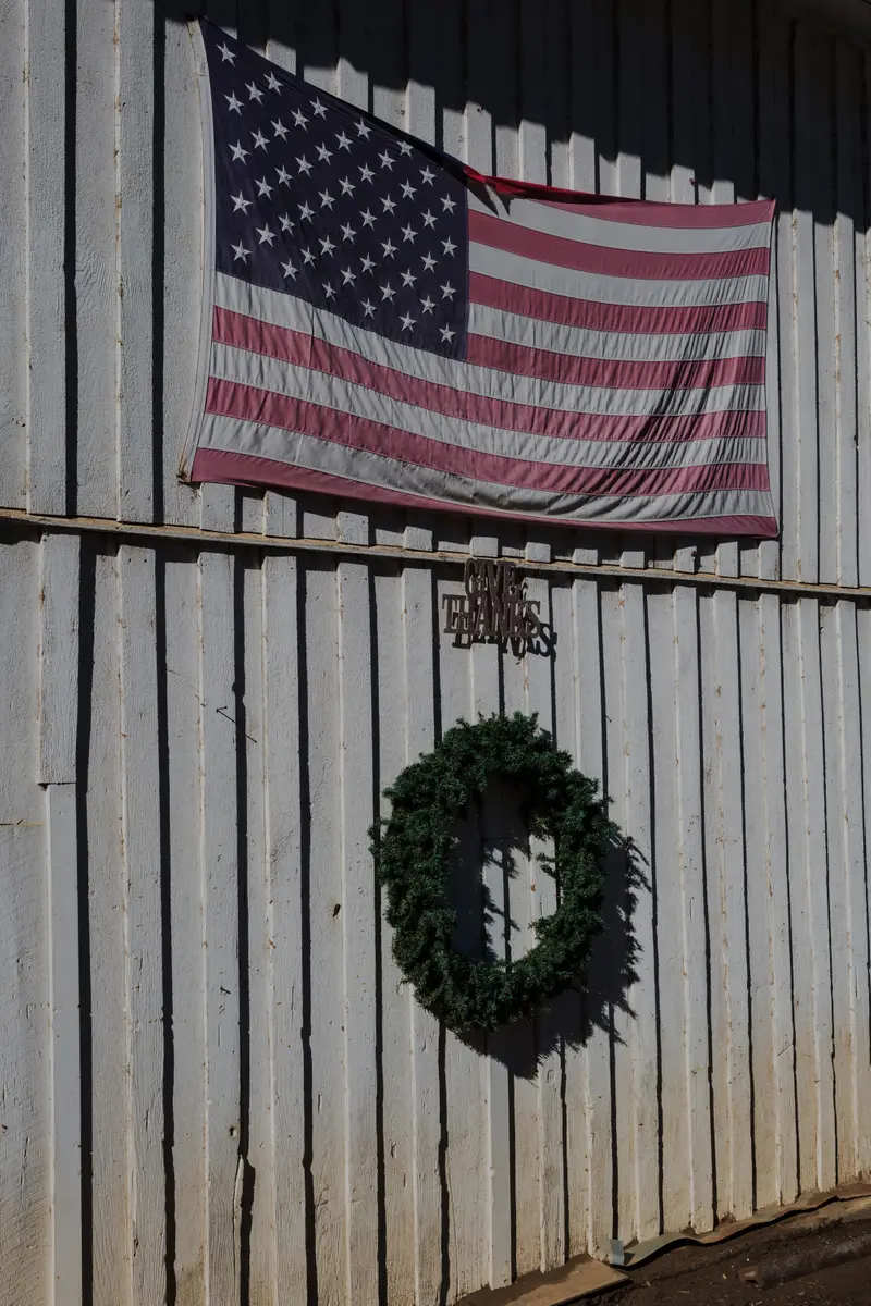 A U.S. flag hangs on a fence above a Christmas wreath and a sign that says “Give Thanks.”