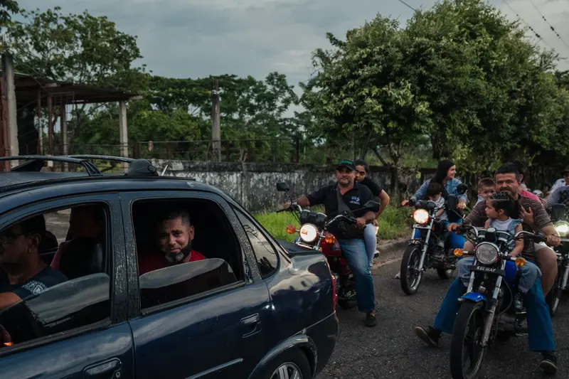 Wilmer sitzt mit unten in einer Limousine in der Rückseite einer Limousine und schaut in die Kamera, während eine große Gruppe von Menschen, darunter eine Reihe von Kindern, auf Motorrädern nach dem Auto zusammengefunden wird.