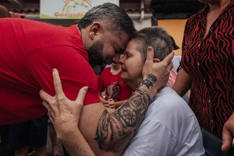 Wilmer hält das Gesicht einer Frau gegen seine eigene Stirn in die Stirn. Die Haare der Frau sind sehr kurz und sie klammert sich an den Armen.