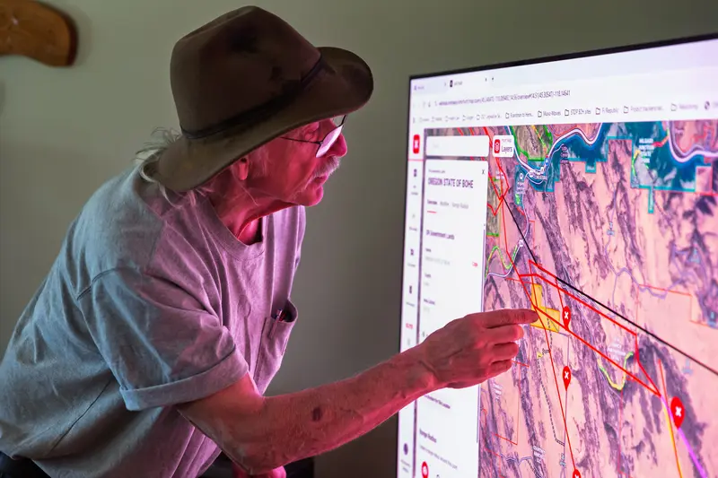Williams leans over an illuminated map on a television screen, which casts a pink glow on his skin and clothing.