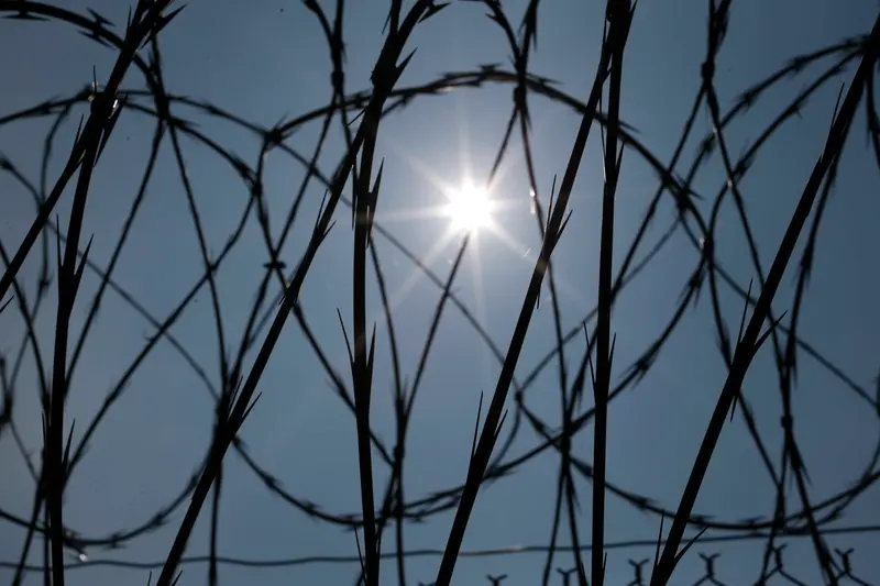 Silhouettes of concertina wire against a blue sky with a bright white sun glowing.