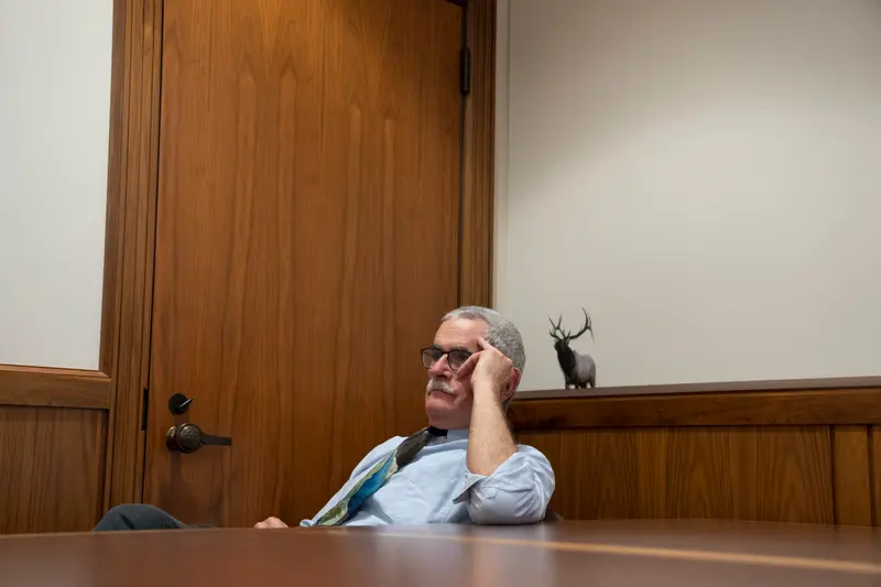 Golden sits in a wood-paneled room with his elbow on a table, leaning his head against his hand.