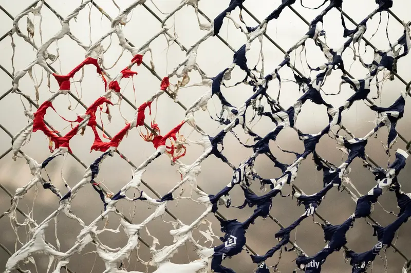 Remnants of red, white and blue plastic drips down a chain-link fence.