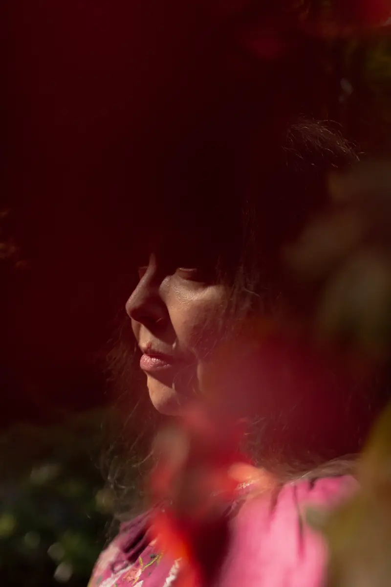 Sutton-Schulman looks off into the distance, her face partially covered by shadowy flowers.