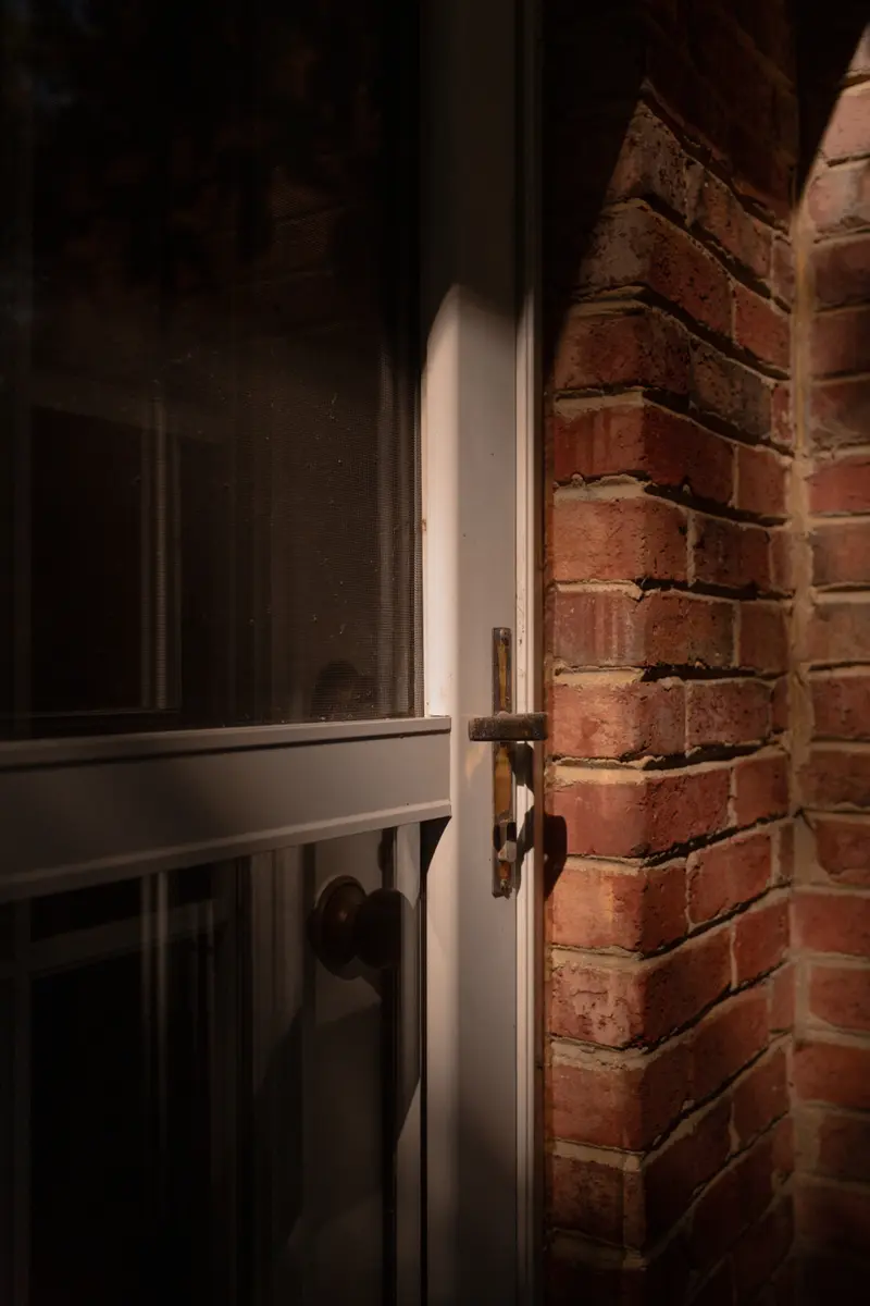 An ominous photograph of the brass handle on a white door to a red brick house.