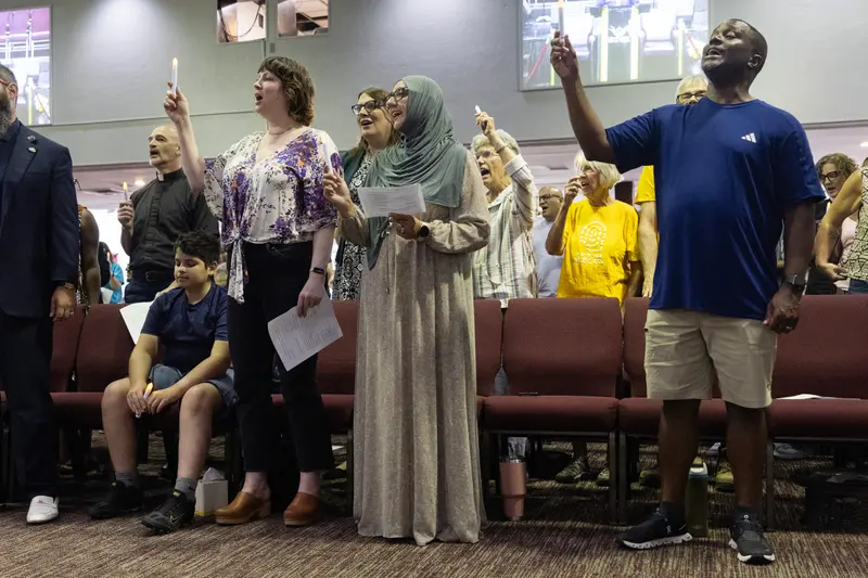 First image: A woman signs a paper in front of a sign reading, “Encourage Cincinnati Children’s to Publicly Support Ayman Soliman.” Second image: People hold candles at a church.