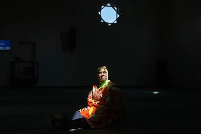 A woman sits in a mosque with a ray of light shining on her.