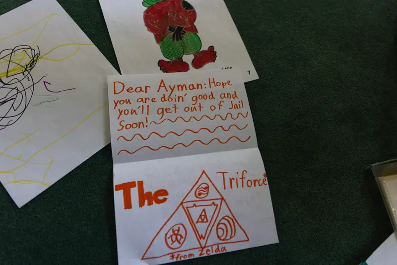 A pile of three letters. The center letter reads, “Dear Ayman: Hope you are doin’ good and you'll get out of Jail soon!” with a drawing below referencing Zelda.