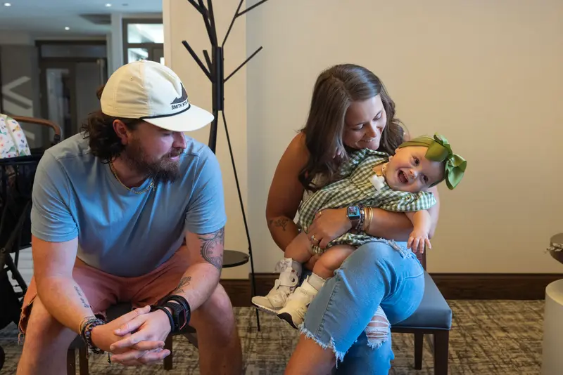 A mother holds a small, laughing child while the father looks on.