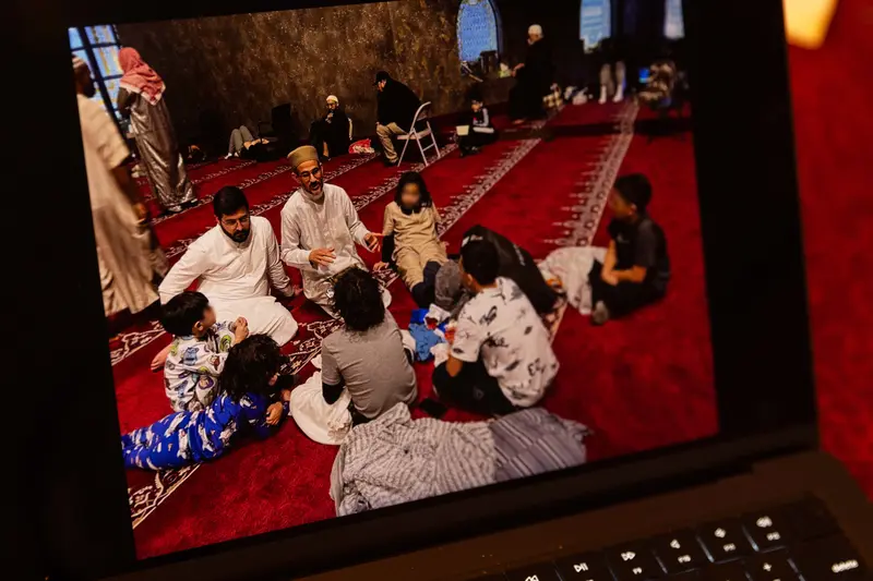 Two men sit with a group of children on a bright red rug.