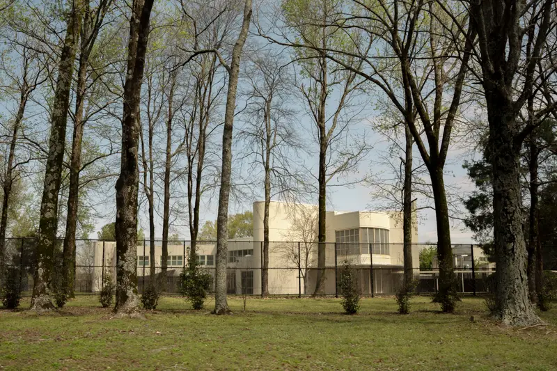 A white, modular building surrounded by a fence and trees.