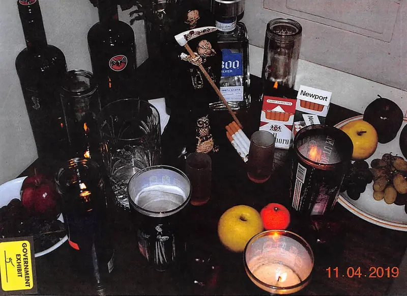 A small wooden table whose surface is crowded with fruit, lit candles, bottles and a grim reaper statue.