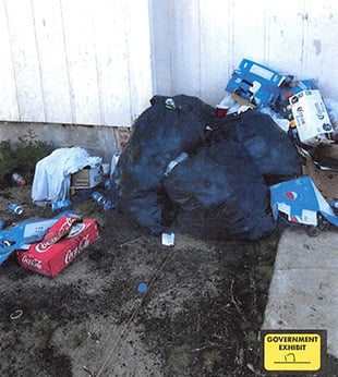 Piles of trash and cardboard boxes against a white-walled building.