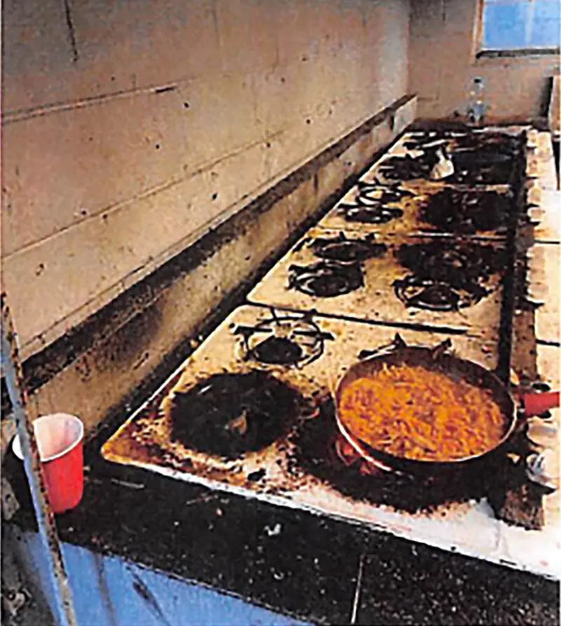 Four dirty, burnt ranges with a pan of food on the burner.