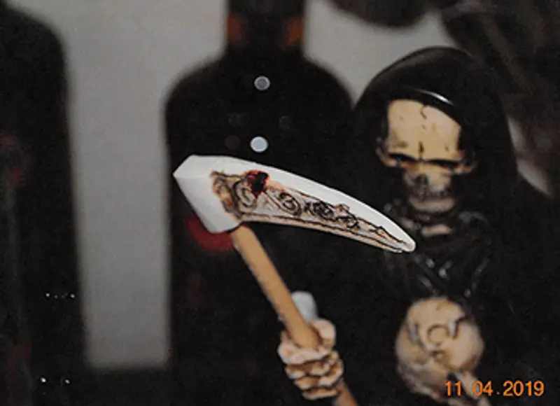 Close-up of the statue showing a dark red-brown smear on the scythe.