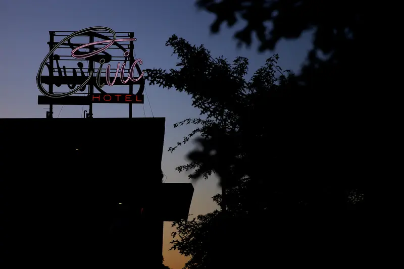 A half-lit neon sign reads “Civic Hotel” on top of a building silhouetted against a sky with a blue-orange gradient.