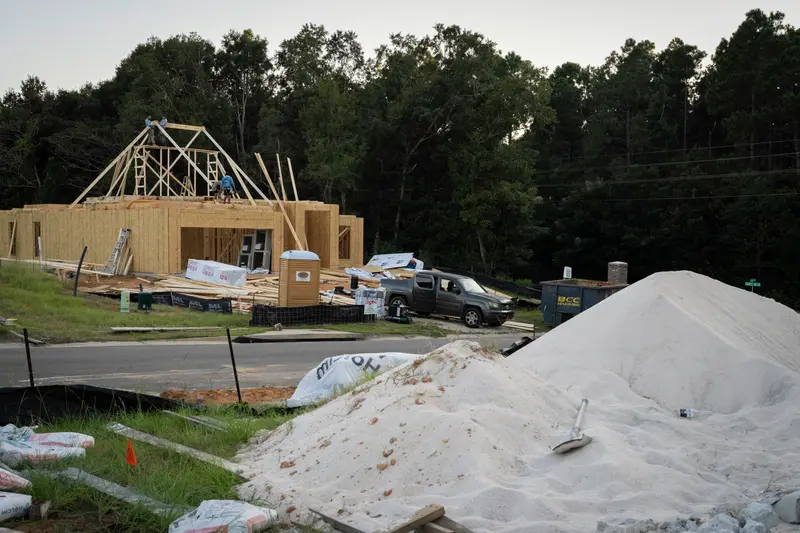 A plywood shell of a house with men on top of it adding roof framing.