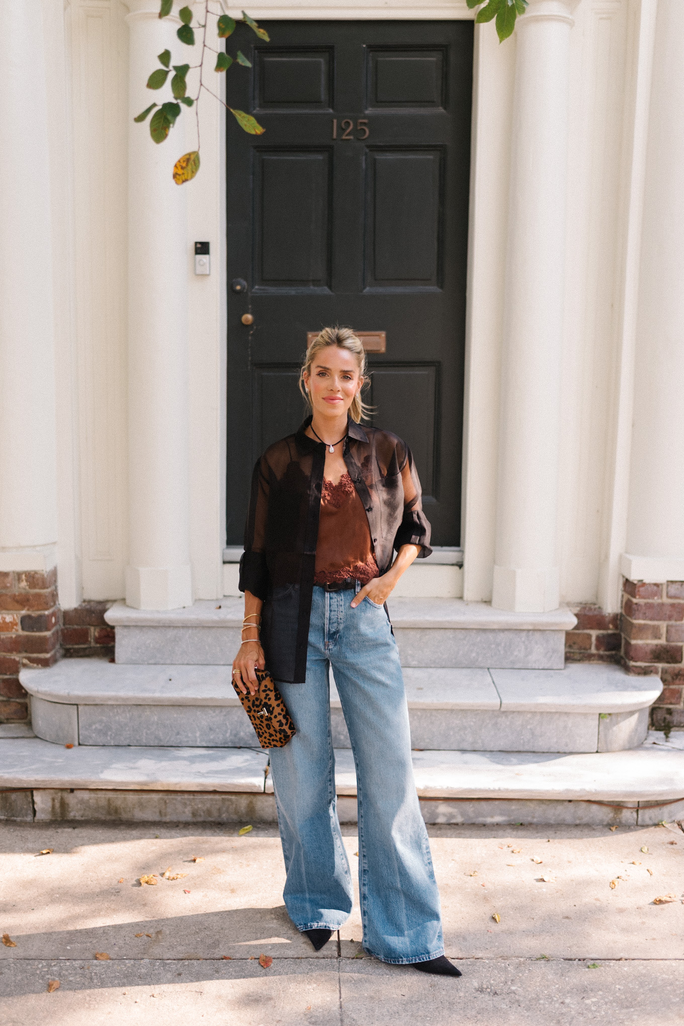 Blouse transparente noire, camisole en soie marron, jean bleu et pochette léopard