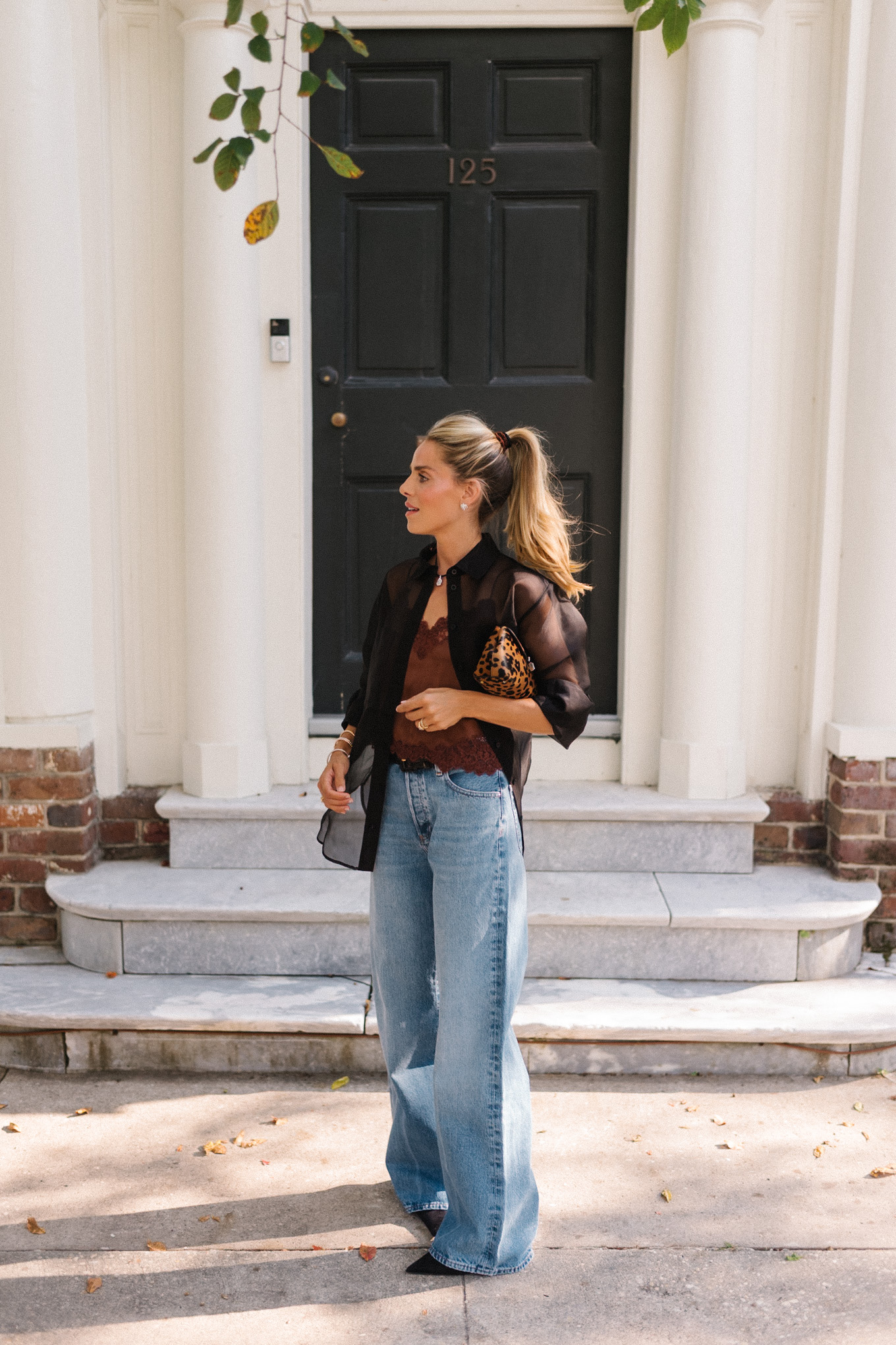 Blouse transparente noire, camisole en soie marron, jean bleu et pochette léopard