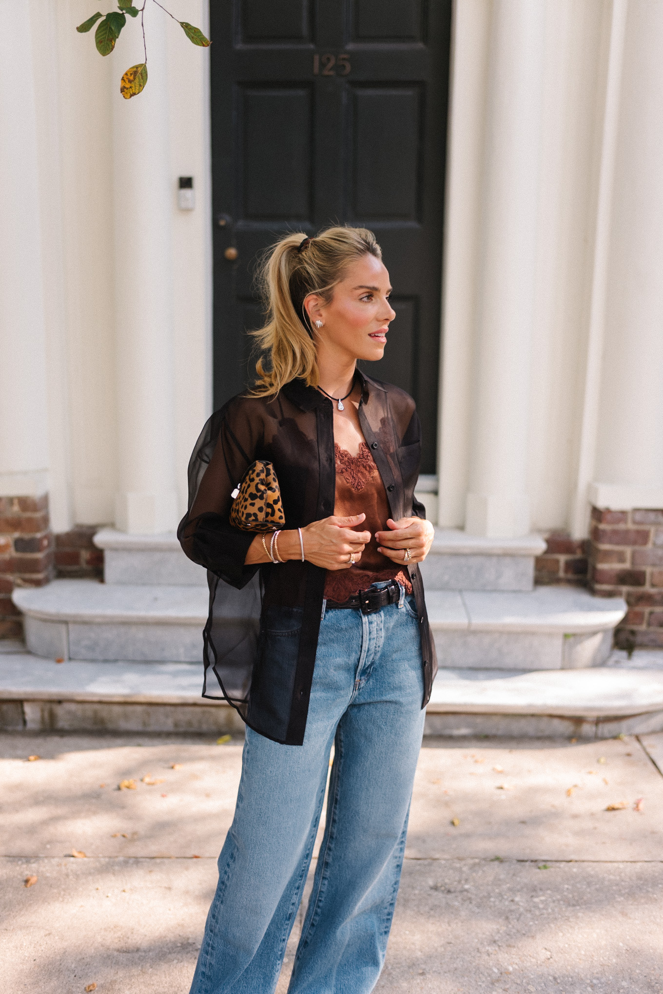Blouse transparente noire, camisole en soie marron, jean bleu et pochette léopard