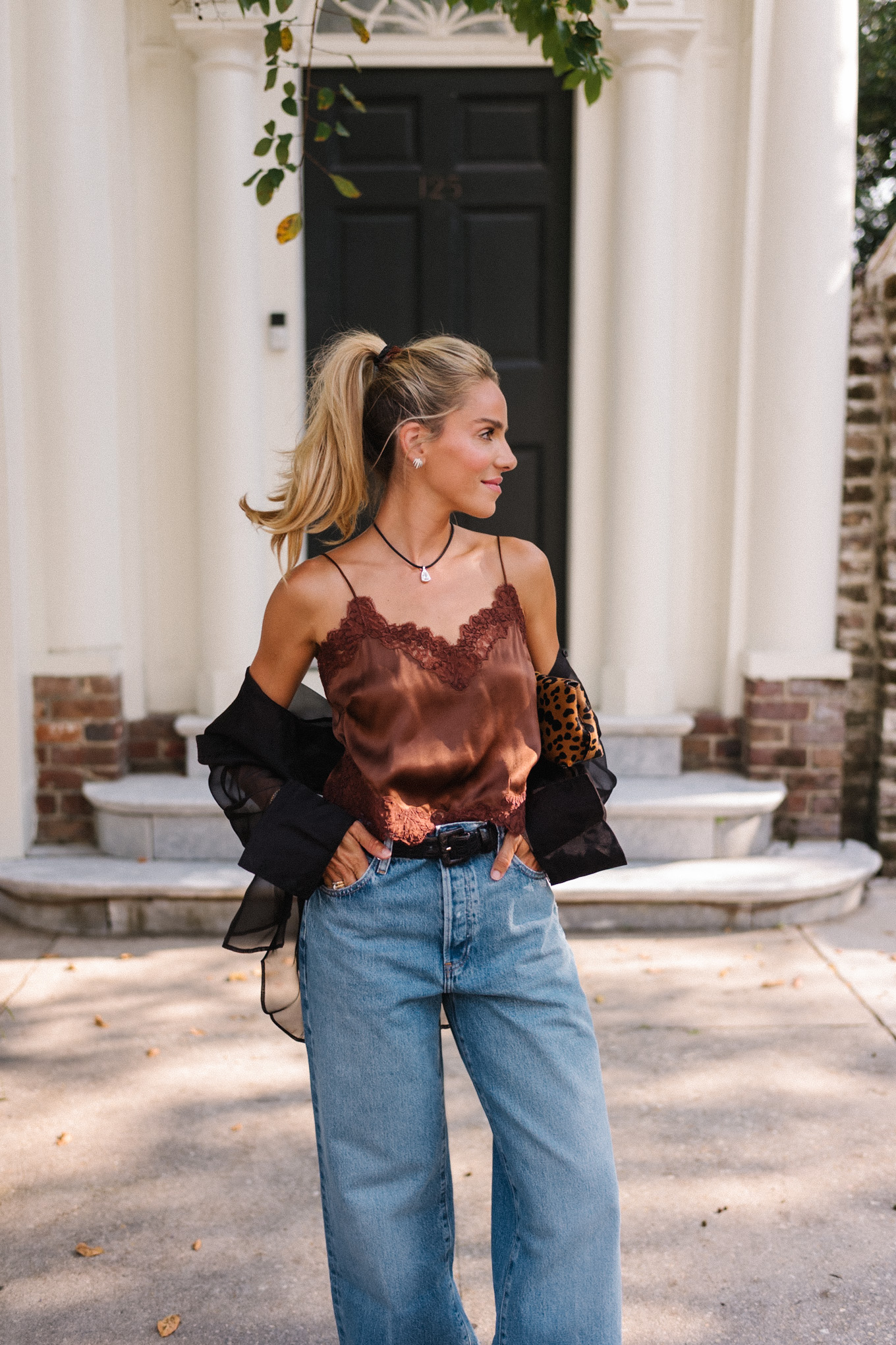 Blouse transparente noire, camisole en soie marron, jean bleu et pochette léopard