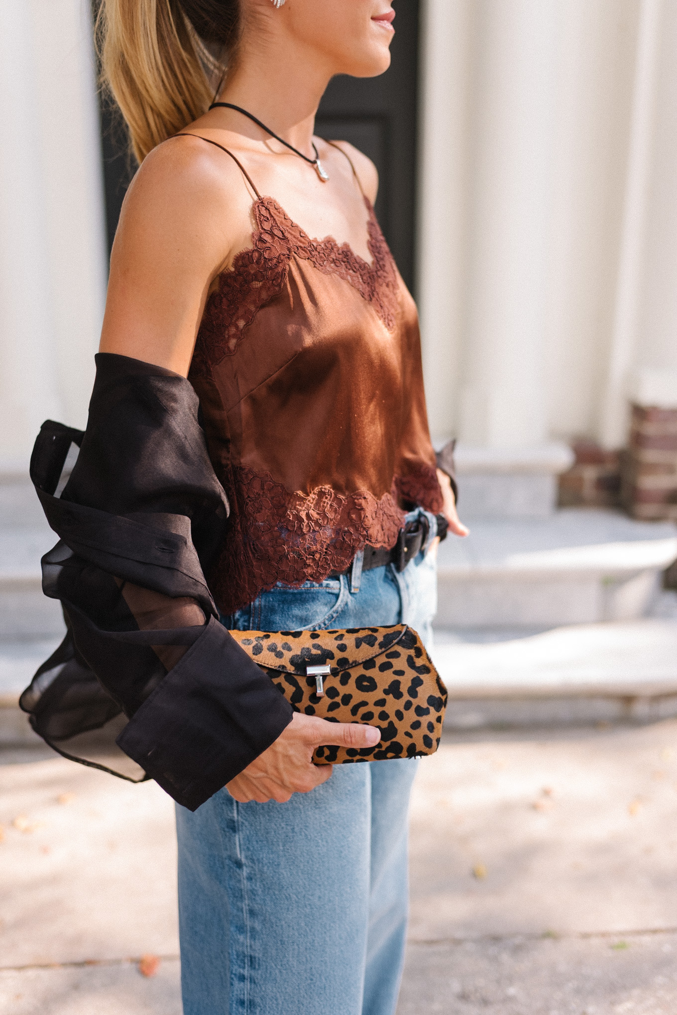 Blouse transparente noire, camisole en soie marron, jean bleu et pochette léopard