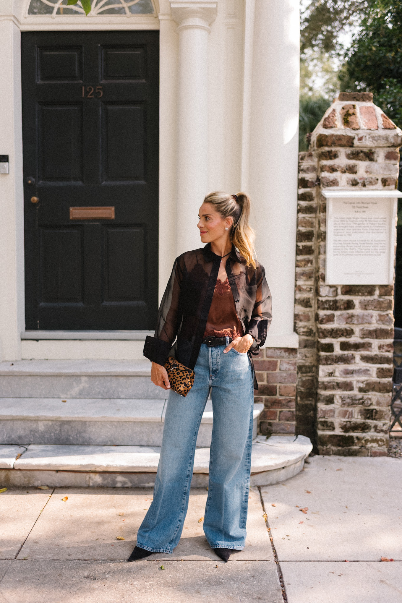 Blouse transparente noire, camisole en soie marron, jean bleu et pochette léopard