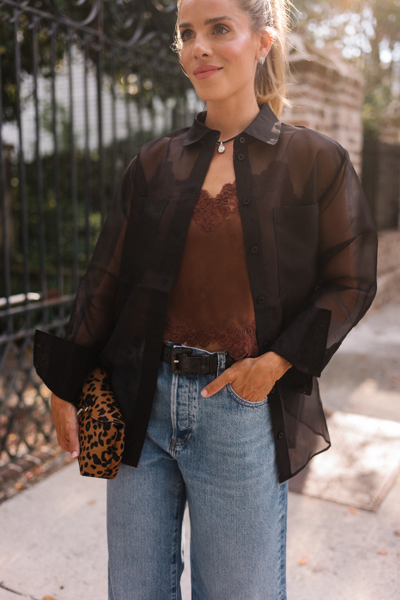 Blouse transparente noire, camisole en soie marron, jean bleu et pochette léopard