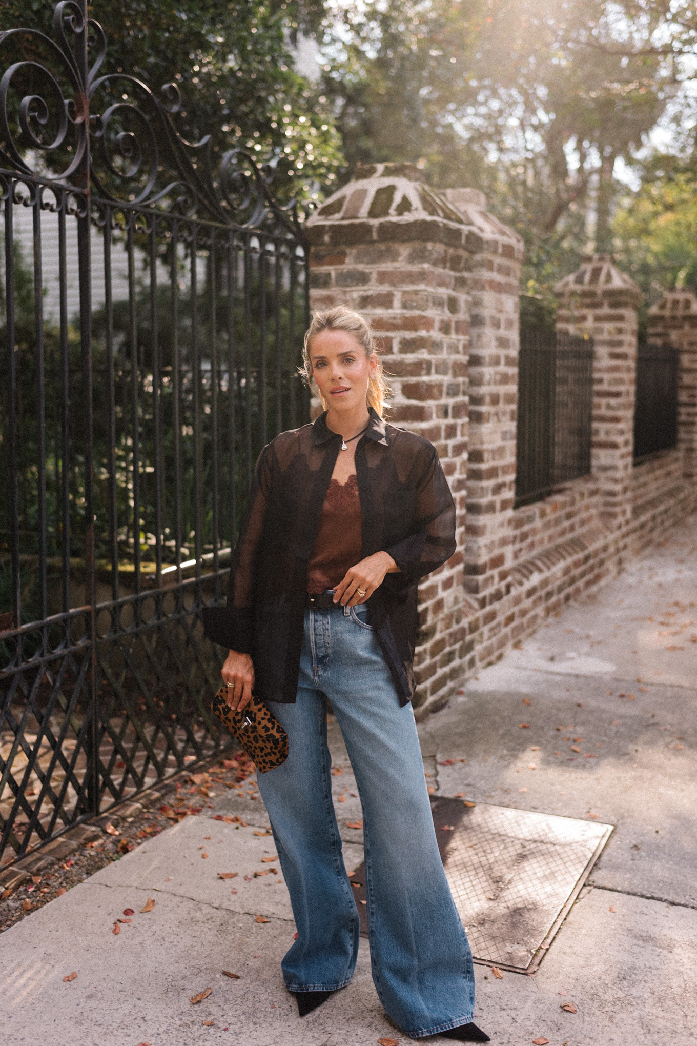 Blouse transparente noire, camisole en soie marron, jean bleu et pochette léopard