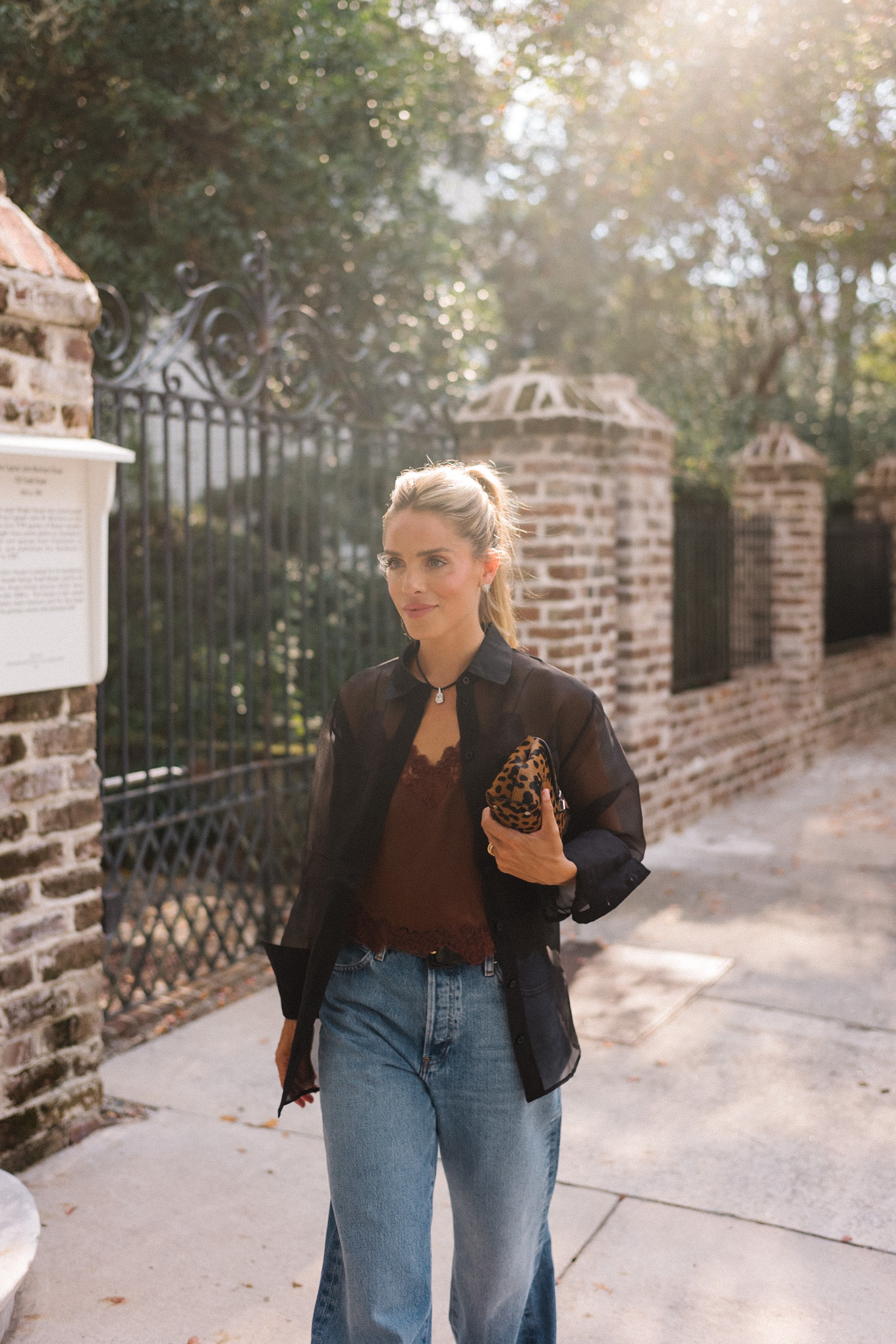 Blouse transparente noire, camisole en soie marron, jean bleu et pochette léopard