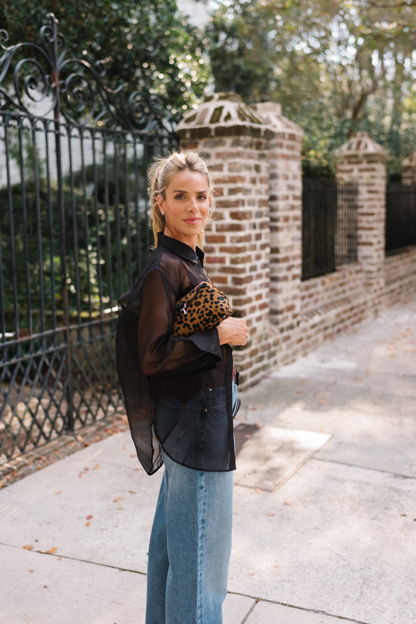 Blouse transparente noire, camisole en soie marron, jean bleu et pochette léopard