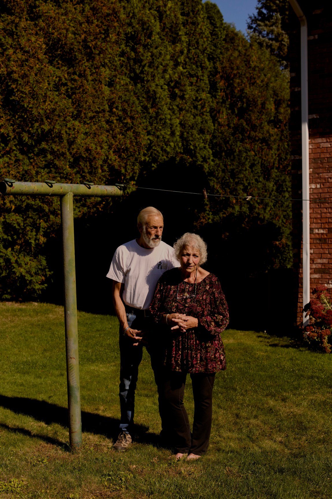 An older couple stand alongside a clothesline in a residential back yard.