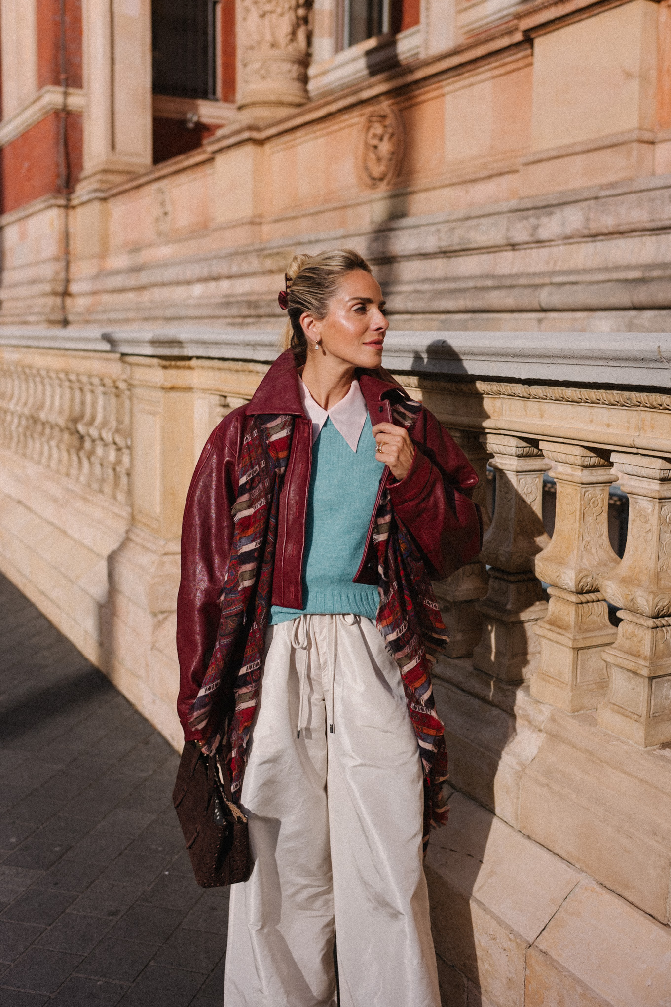 veste en cuir marron, écharpe rayée, pull turquoise, chemise boutonnée blanche, pantalon large crème