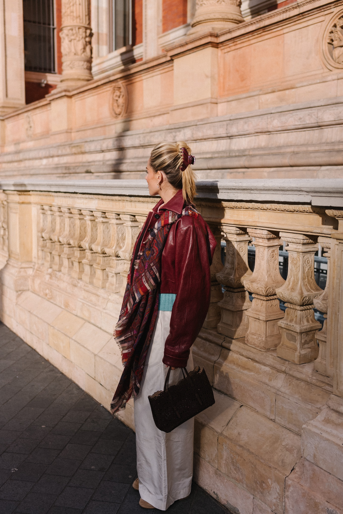 veste en cuir marron, écharpe rayée, pull turquoise, chemise boutonnée blanche, pantalon large crème
