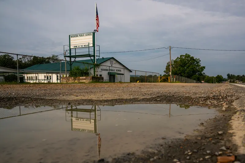 The Nashoba Public School marquee is seen reflected in a puddle alongside a rural road in Oklahoma.