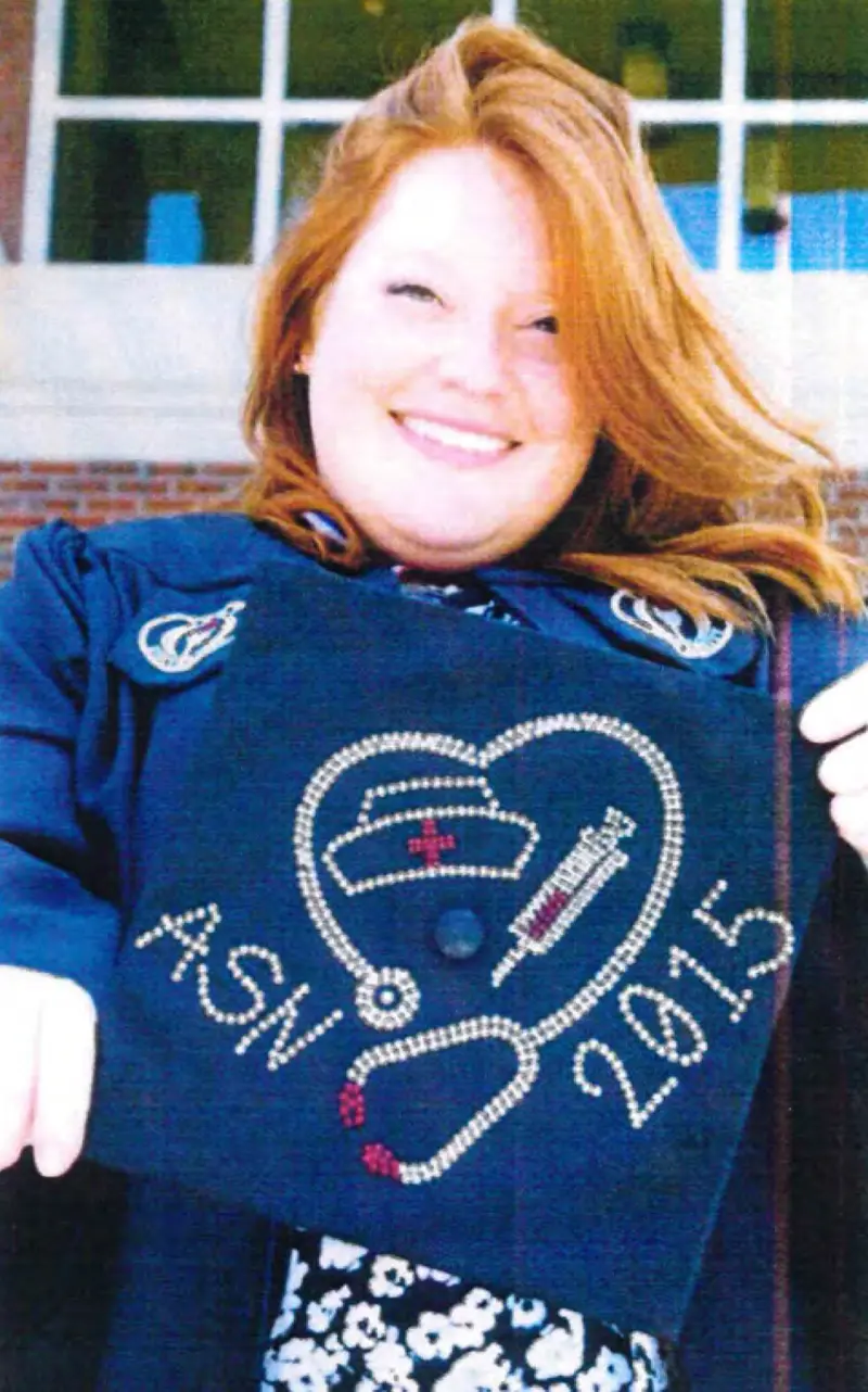A smiling woman with red hair wears a graduation gown and holds a mortarboard decorated with a stethoscope, syringe, nurse’s hat and the words “ASN 2015.”