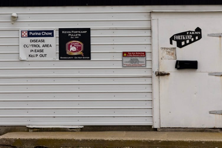 Biosecurity signs reading, “Disease control area. Please keep out,” and “You are entering a bio-secure area,” are posted on the side of a white metal barn.