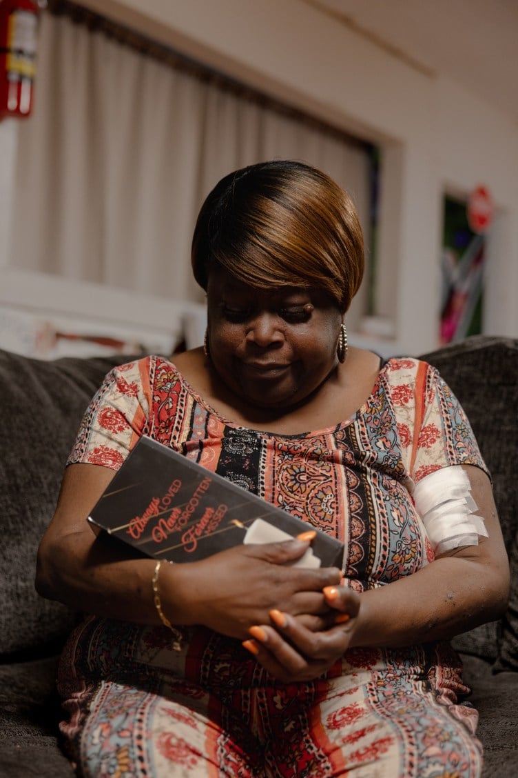 A woman tenderly cradles an urn inscribed with the words “Always loved, never forgotten, forever missed.”