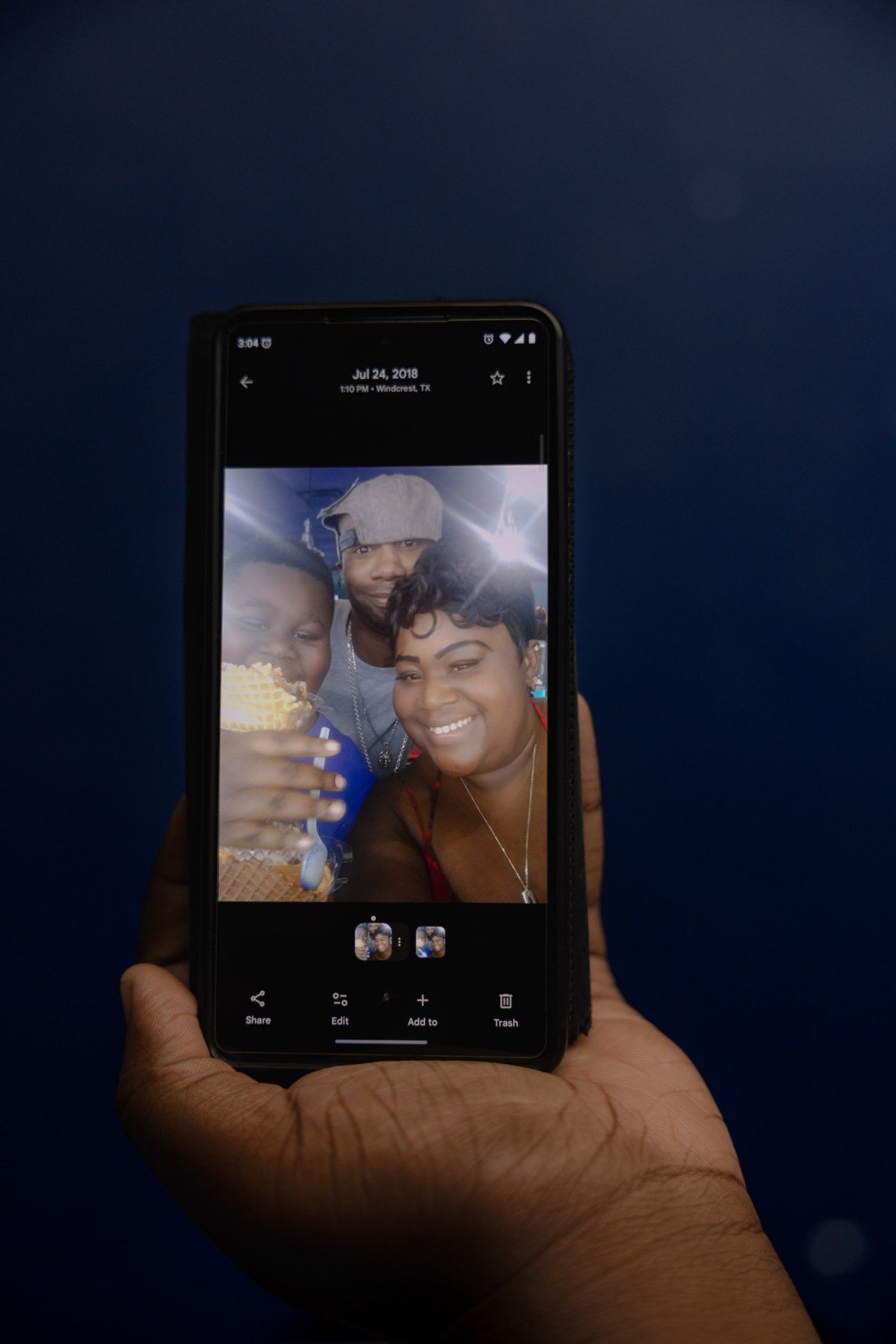 JJ’s hand holds a phone showing a photo of him, his mom and his stepdad smiling at the camera.