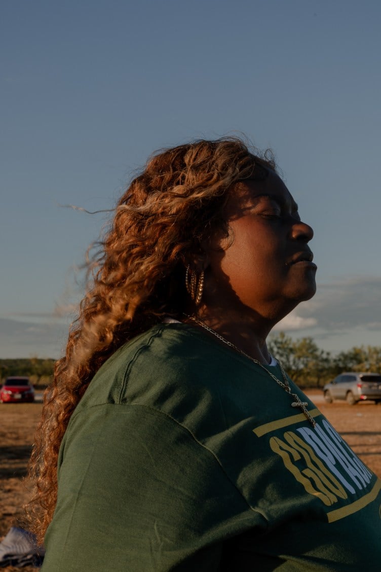 A woman, whose long curly hair blows in the wind, closes her eyes and looks toward the sky.