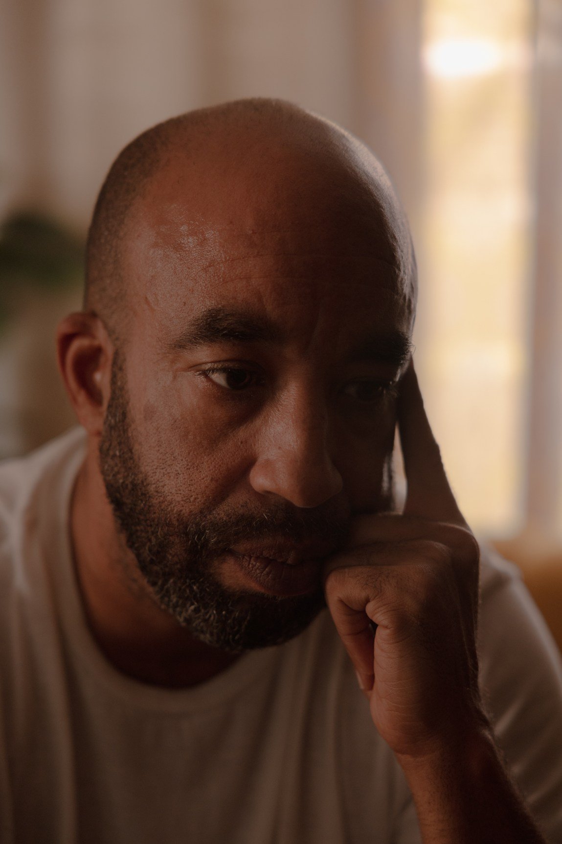 A man rests his head in his hand, looking longingly off camera.