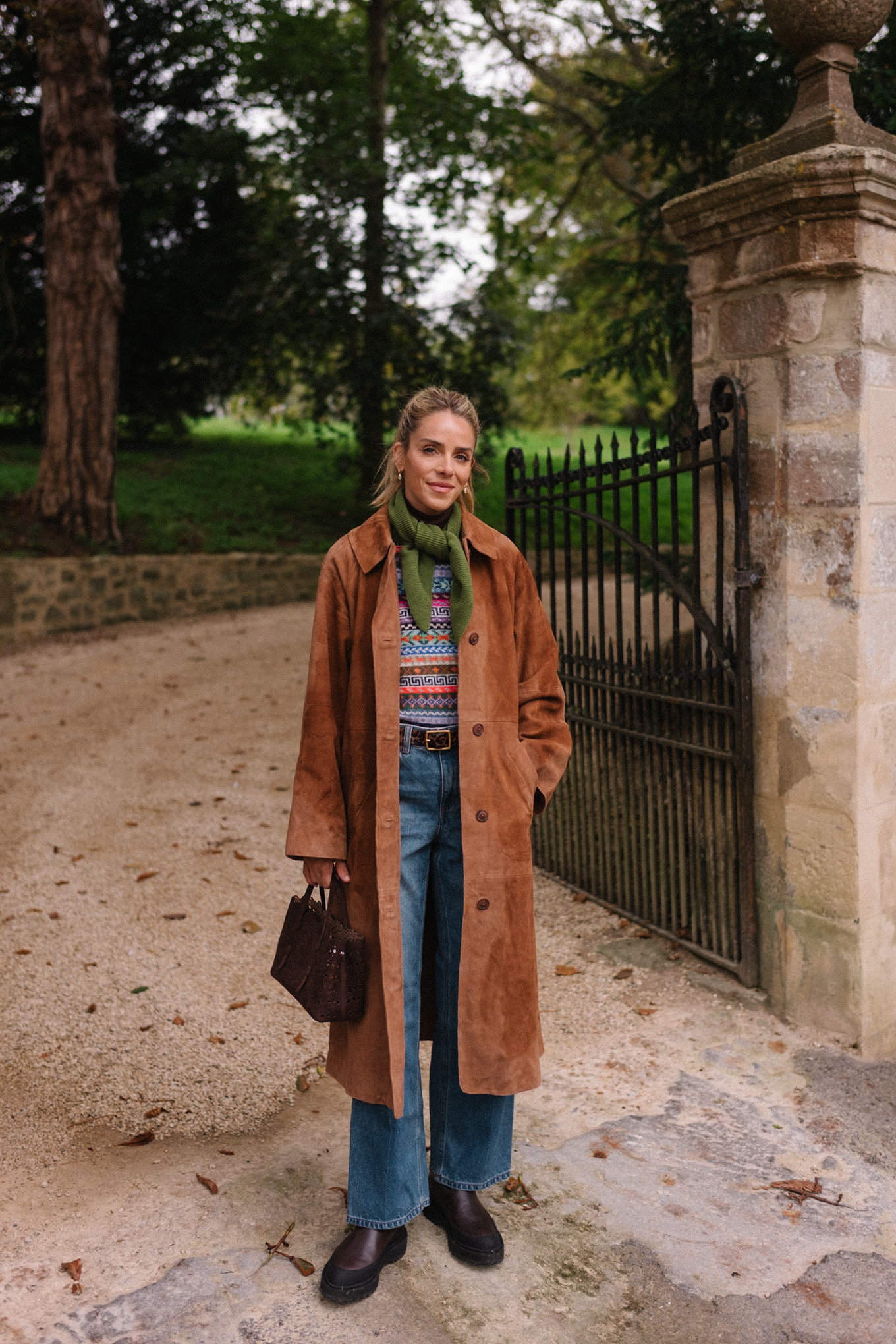 Manteau d'hiver en daim marron, pull en jacquard, gilet, écharpe verte, jean bleu, bottes marron